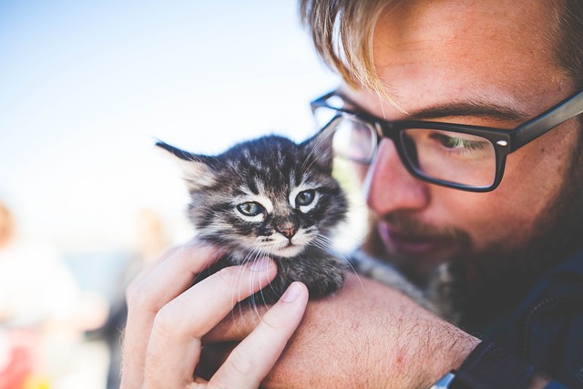 A man wearing glasses holding a tiny black and white kitten
