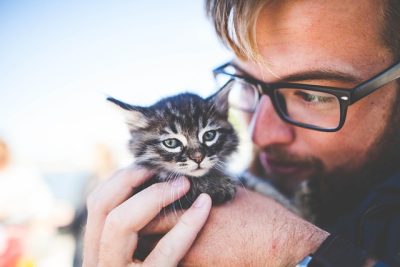 Man wearing glasses holding a small black and white kitten