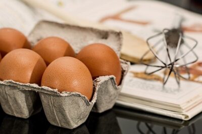 Carton of eggs, whisk, and cookbook on a counter
